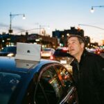 Hombre mirando con asombro un iPad olvidado en el techo de su coche al atardecer.